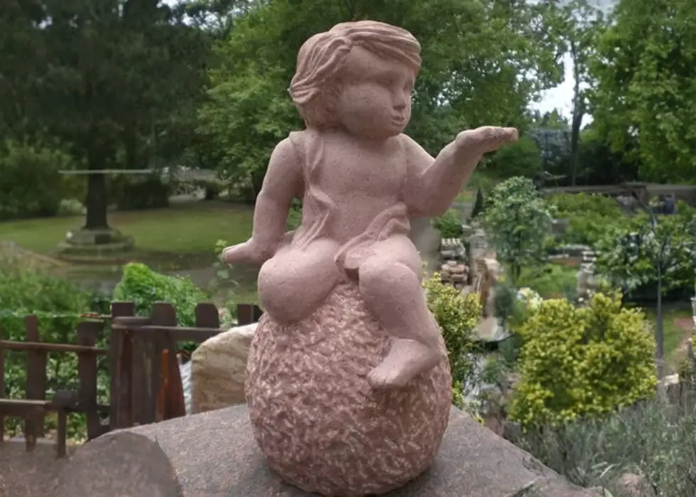 Kinderfigur aus Stein sitzt auf einer Kugel im Garten
